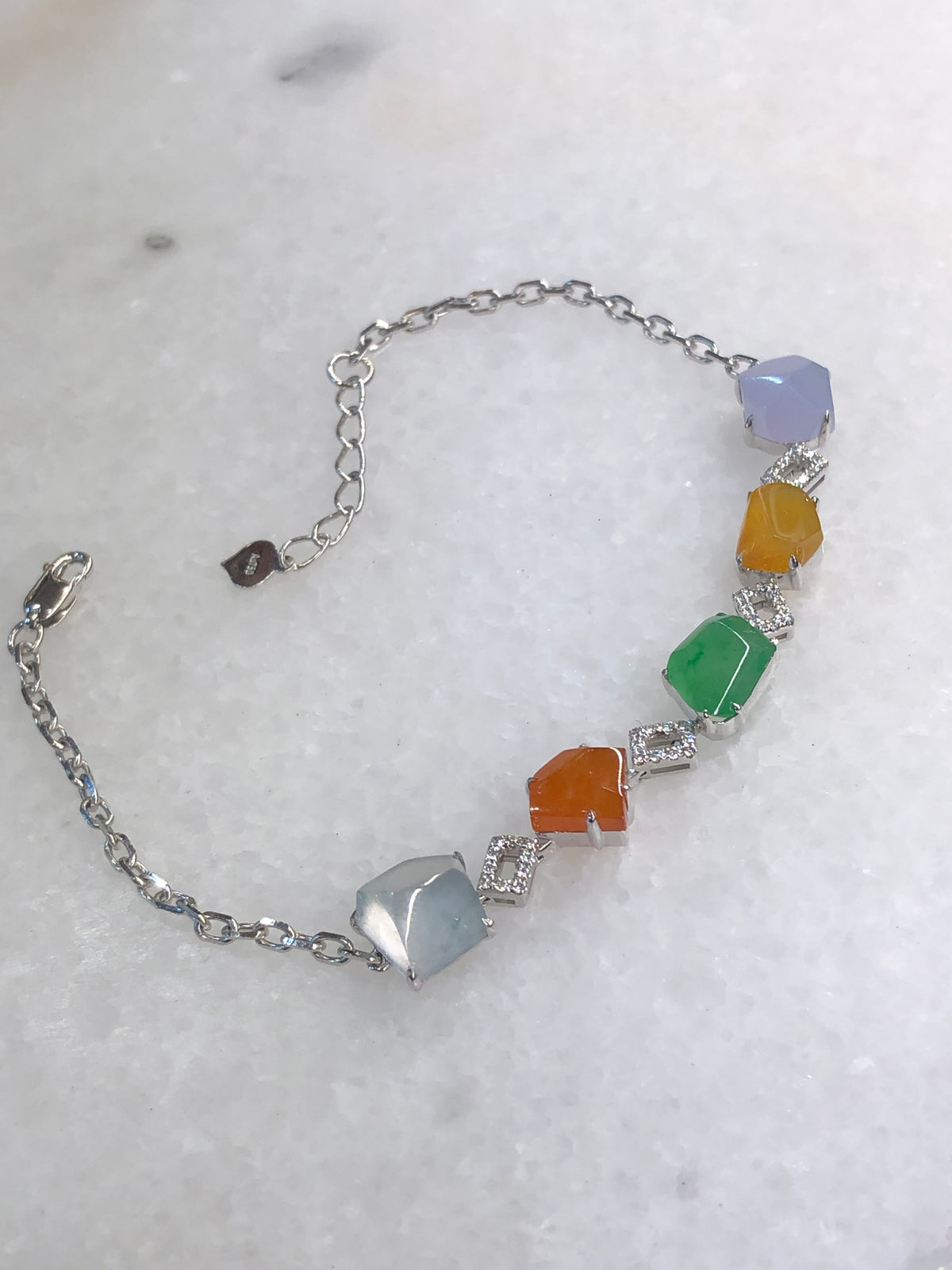 Multi-coloured natural Type A faceted jadeite bracelet featuring green, orange-red, yellow, lavender and icy white jade with diamond-set geometric links in 18K white gold.
